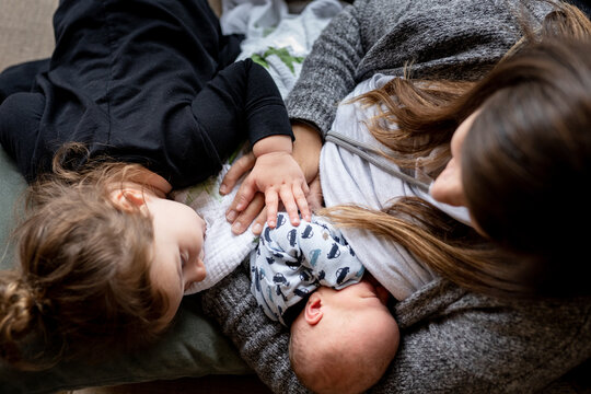 Top down view of mom breastfeeding baby while toddler snuggles them.