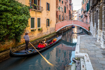 Gondola with tourists sails on old canal under medieval Bridge of Sighs, Venice, Italy. Famous historical landmark of Venice. Romantic water trip across Venice. 