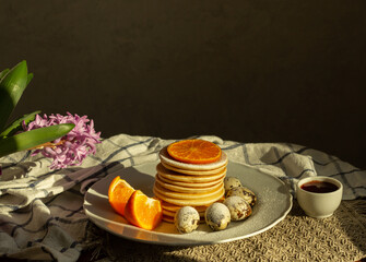 A delicious breakfast is served on the table, pancakes, dessert, quail eggs, tangerine slices,orange, with a hyacinth flower in the background