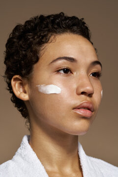 Young woman applying cream on face
