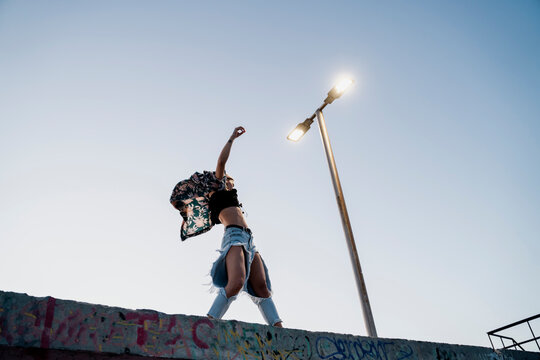 Young stylish woman standing on top of wall dancing