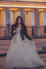 Naklejka premium A beautiful bride in a wedding dress and a leather jacket with a bouquet of flowers. Wedding concept. Evening photography
