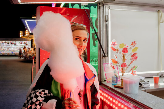 Trendy woman holding a cotton candy in fairground next to sweets stand shop