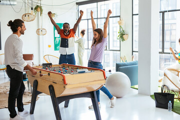 Diverse colleagues playing foosball in workplace
