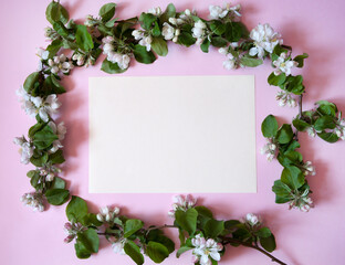 Flower arrangement. Blank paper surrounded by spring branches of a blooming apple tree on a pastel pink marble background. Free space. Top view.