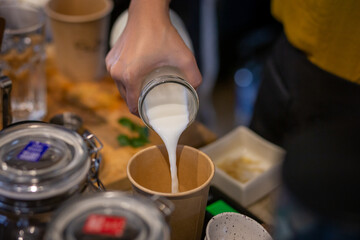 Barista pours milk in a paper cup. Drink shop employee in a coffee shop