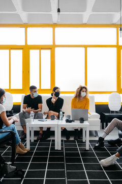 group of diverse coworkers wearing face masks chilling and talking during coffee break in a modern and bright workspace