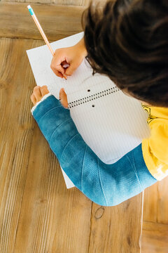 Boy with a blue cast doing schoolwork.