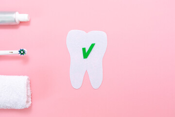 Hygiene of the oral cavity. The silhouette of a tooth cut out of felt, next to an electric toothbrush, towel and toothpaste. Flat lay. Pink background. Copy space