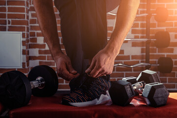 Fototapeta na wymiar Fitness motivation and muscle training concept. Man in sneakers tying shoelaces in sunlight. Athlete starting exercise with dubbell weight.