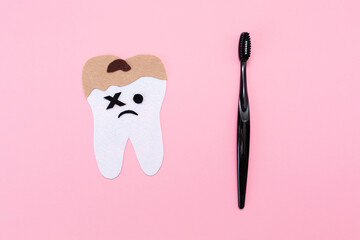 A plastic toothbrush and a felt-cut out sad tooth with decay. Flat lay. Pink background. Copy space. Concept of hygiene of the oral cavity