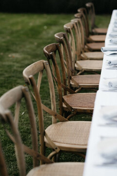 Long row of rustic wooden chairs outdoors in a table setting
