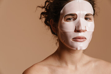 Half-naked woman looking at camera while posing in facial mask