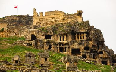 Lycian rock hewn tombs in stone cliff and ruined castle on top in ancient settlement of Tlos...