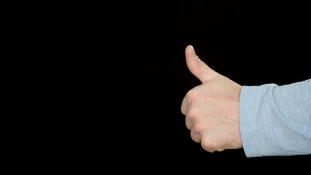Close-up view of male hand showing thumb up on black background. Cropped shot of man showing thumb up gesture and approving something isolated on black
