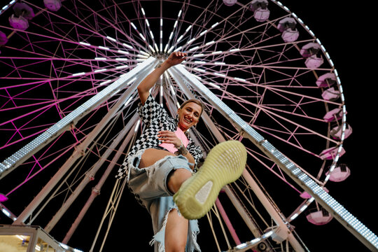 Trendy woman having fun and dancing in a fairground in front of a ferris wheel