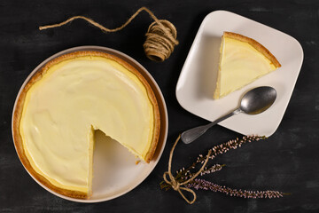 Traditional New York cheesecake with cream cheese and sour cream layer with one slice on white plate