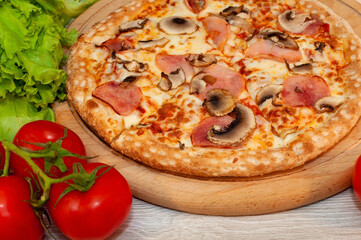 Pizza with ham, mushrooms and cheese on a board with tomatoes and green salad