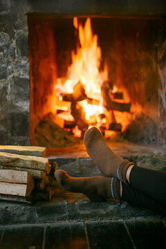 The girl warms her feet near the fireplace