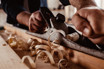 Carpenter's hands planing a plank of wood with a hand plane - obrazy, fototapety, plakaty