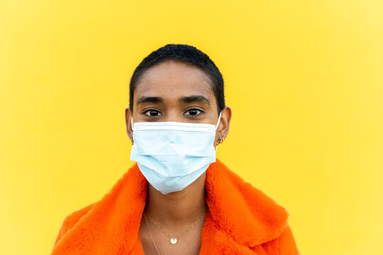 Portrait of young short hair woman wearing mask in front of yellow wall