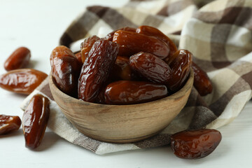 Bowl of dried dates on kitchen napkin on white wooden background