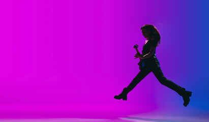 Silhouette of young female guitarist isolated on gradient background in neon.