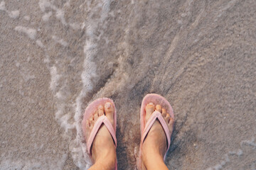 Fototapeta na wymiar Woman feet wear slippers stand on sand tropical beach with sea water splash.