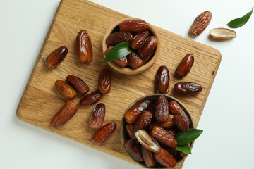 Board with bowls of dried dates on white background