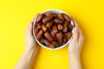 Female hands hold bowl of dried dates on yellow background