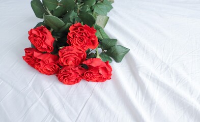 7 red roses lie on the white bed linen like a fallen bouquet use as a background or a postcard