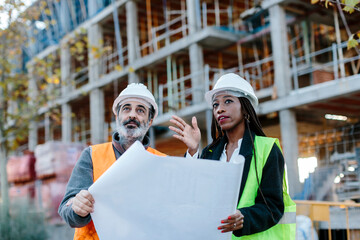 Woman engineer giving instructions to construction worker based on blueprints.