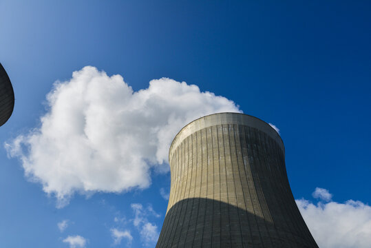 Contre-plongée d'une tour d'une centrale nucléaire d'où sort de la vapeur d'eau en fumée blanche sur fond de ciel bleu
