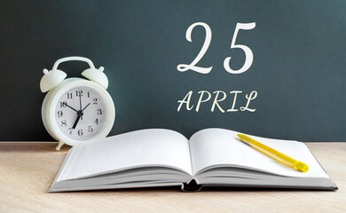 April 25. 25-th day of the month, calendar date.A white alarm clock, an open notebook with blank pages, and a yellow pencil lie on the table.Spring month, day of the year concept