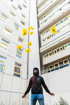 Young urban man looking up to the sky throwing flowers in front of flat buildings