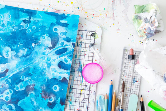 Painting a watercolour with associated equipment and colourful paint drops mess.
