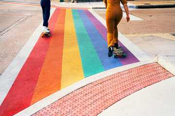Pride. A couple of gay friends rolling longboard on heels boots over a rainbow flag crosswalk.