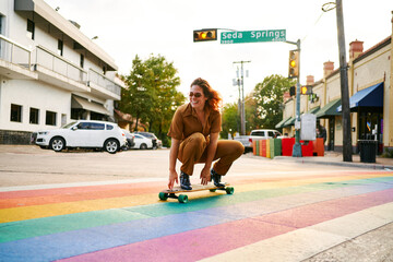 Young girl skating over a pride flag crosswalk.
