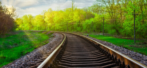 Morning landscape on the railway tracks. The sun's rays are the green grass and the rails on which the train travels. Trees along the railway.