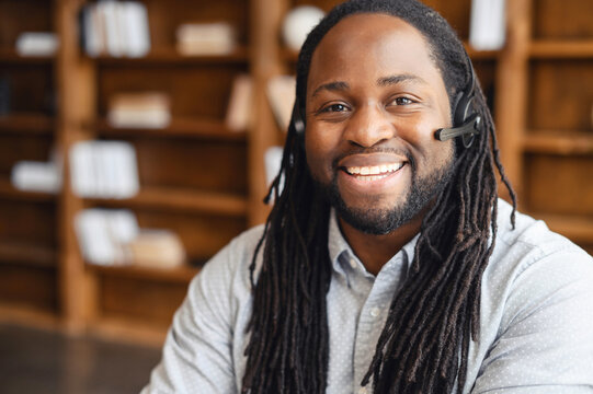 African american operator with long dreadlocks and headset, looking at camera, working in callcentre on support hotline in modern office with copy space, portrait of positive agent in conversation