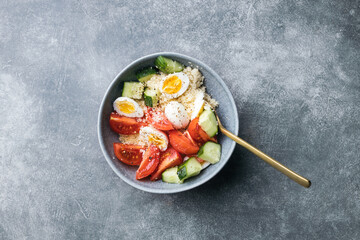 Cous cous salad bowl with cucumber, cherry tomato and quail eggs on stone table. Top view.