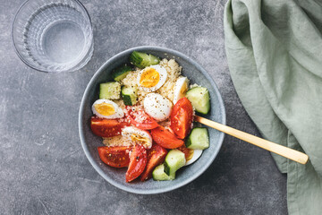 Cous cous salad bowl with cucumber, cherry tomato and quail eggs with glass of water on stone table.