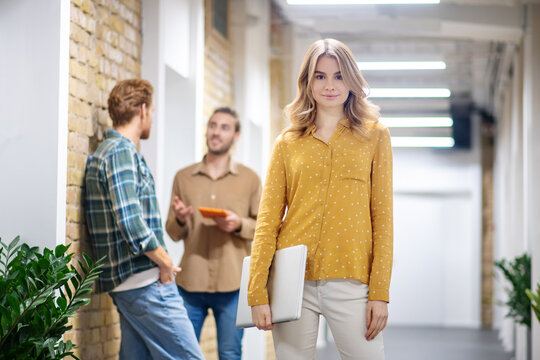 Blonde Woman Standing In The Corridor While Her Colleagues Talking Behind Her Back