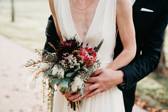 Bride and groom holding a beautiful wedding bouquet with white and red details