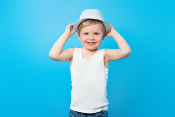 Happy summer boy in white t-shirt and hat on a blue background with copy space. Tank top mockup. Summer kid, travel concept