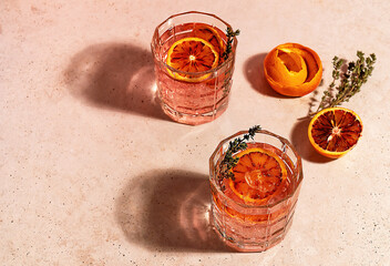 Pink gin cocktail with red blood orange and ice in sunny day. Trendy hard reflections.