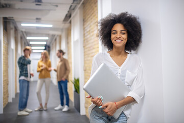 Curly-haired standing near the wall with a laptop in hands