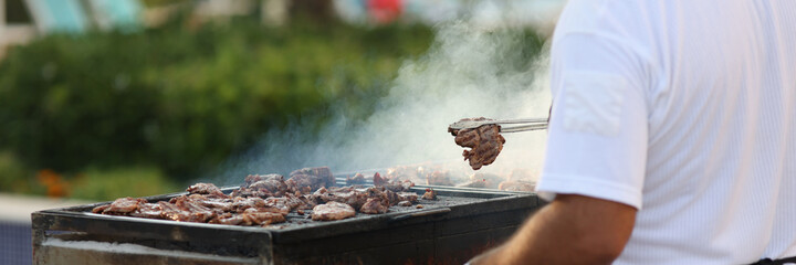 Chef removes fried hot cuts of meat with tongs from grill and places in plate.