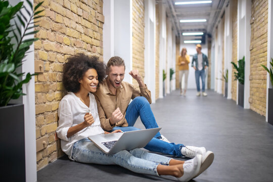 Two colleagues sitting on the floor in the corridor and discussing something