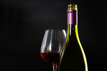 Wine bottle and glass with red wine on dark glossy background.